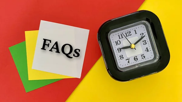 Preguntas frecuentes - mensaje en bloc de notas blanco. Con despertador, fondo rojo y amarillo. Concepto empresarial. — Foto de Stock