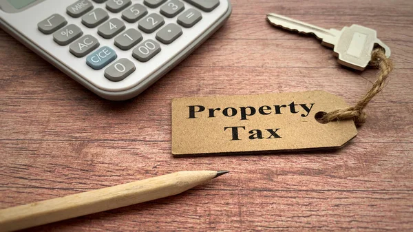 Property Tax text on keychain with calculator, pencil and wooden desk background. Property tax concept. — Stock Photo, Image