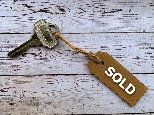 带有房屋钥匙和木制桌子背景的褐色标签上的文字-销售.财产概念. — 图库照片