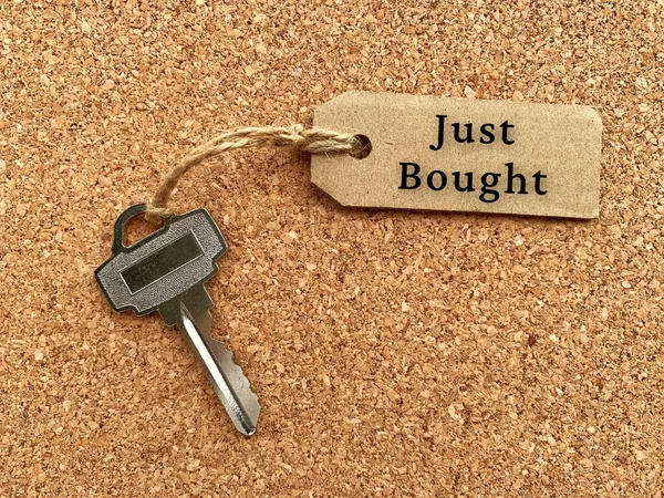 带有房屋钥匙和木制桌子背景的褐色标签文字- -刚刚买的。财产概念. — 图库照片
