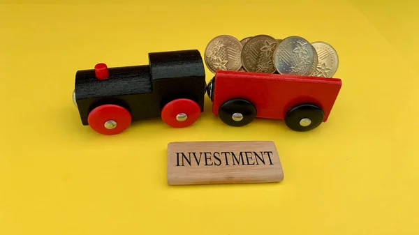 Игрушечный поезд перевозит золотые монеты с инвестиционным словом на деревянном блоке. Концепция инвестиций и бизнеса. — стоковое фото