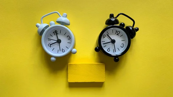 White and black alarm clock on yellow background with small wooden. Copy space concept — Stock Photo, Image