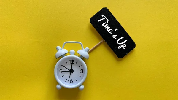 Alarm clock on yellow background with text on small black signage - Time is up. — Stock Photo, Image