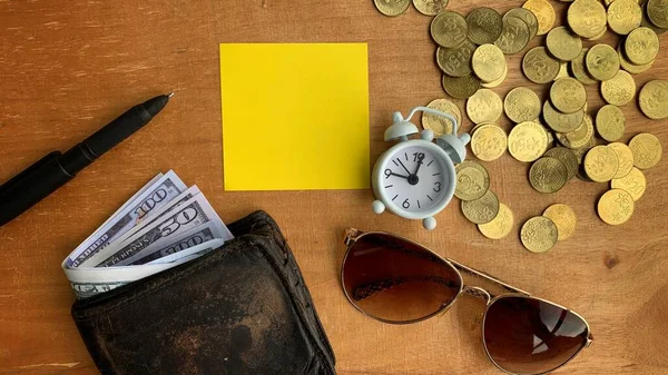 Vue du dessus du portefeuille, des billets de banque, des pièces de monnaie, du réveil, des lunettes et du stylo sur un bureau en bois. Concept d'espace de copie — Photo