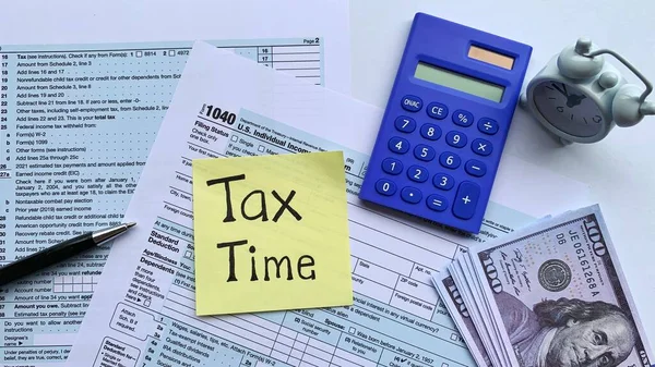 Horní pohled na text na žlutém notepadu - Daňový čas. S daňovým formulářem, bankovkami a modrou kalkulačkou na pozadí. — Stock fotografie