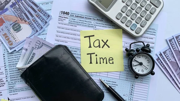 Horní pohled na text na žlutém notepadu - Daňový čas. S daňovým formulářem, bankovkami, kalkulačkou a pozadím budíku. — Stock fotografie