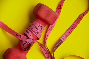 Sarı zemin üzerindeki dambıl ve mezuranın üst görünümü - Fitness ve kilo kaybı konsepti