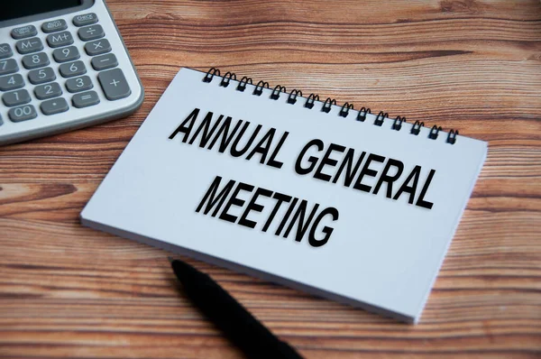 Annual general meeting text on notepad with calculator, pen and wooden table background. Business concept
