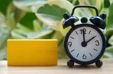 Siyah alarm saati ve bulanık doğa arka planında izole edilmiş boş sarı tahta blok. Saat 2 'ye ayarlandı. Boşluğu kopyala.