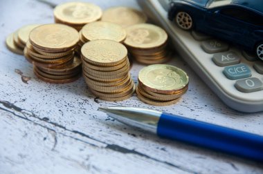 Gold coins, calculator, blue car toy and pen on wooden background. Selective focus on coins. Finance and copy space concept