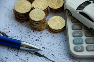 Gold coins, calculator, white car toy and pen on wooden background. Selective focus on coins. Finance and copy space concept