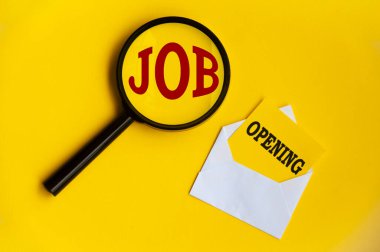 Job opening tax on magnifying glass and notepad in an envelope on yellow background. Employment concept