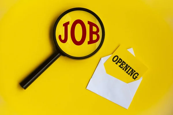 Job opening tax on magnifying glass and notepad in an envelope on yellow background. Employment concept