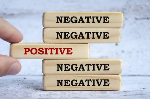 Negative and positive text on wooden blocks with hand placing a wooden block in the middle. Conceptual