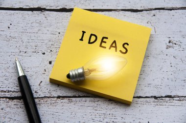 Not defterinde ampul olan fikirler metni. Ahşap masa ve kalem arkaplanı