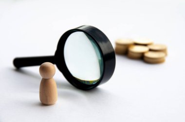 Wooden doll looking through magnifying glass for wealth. Business concept and copy space.