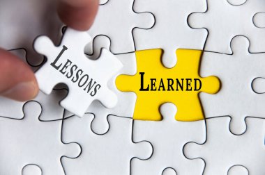 Lessons learned text on Jigsaw Puzzle with one hand holding a missing jigsaw pieces. clipart