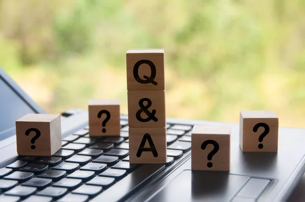 Question and answer text on wooden block on top of laptop with blurred nature background. Question and answer concept