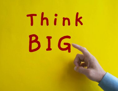 Hand pointing Think Big text on yellow cover background. Thinking concept