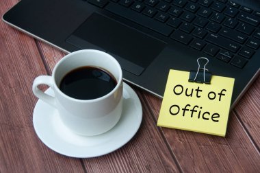 Kahve fincanı ve dizüstü bilgisayar ahşap masanın üstünde, sarı not defteriyle ofis dışında. İş konsepti