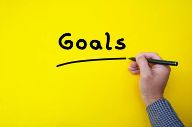 Businessman writing goals on yellow cover background. Business goal concept