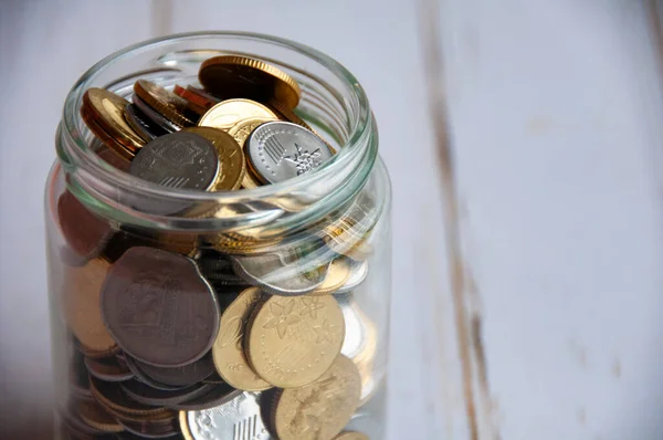 Close up of coins in a jar on wooden table with customizable space for text or ideas. Copy space and business concept
