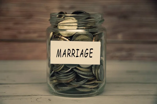 Marriage label on coin jar on top of wooden desk with blurred background. Relationship concept