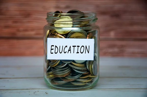 Education label on coin jar on top of wooden desk with blurred background.