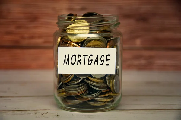 Mortgage label on coin jar on top of wooden desk with blurred background. Mortgage concept