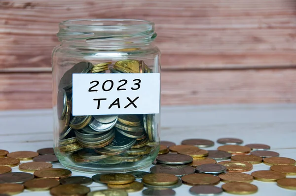 2023 tax label on coin jar on wooden table. Taxation concept