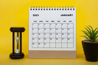 Ocak 2023 masa takvimi, masa bitkisi ve sarı arka planda dakikalar camı. Takvim kavramı