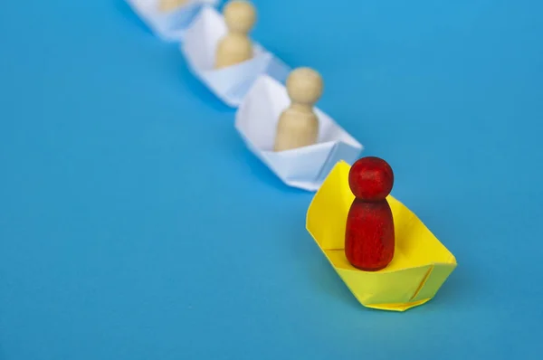 Leadership Concept - Red wooden figure on yellow paper ship origami leading the rest of the figure on white paper ship. Copy space.