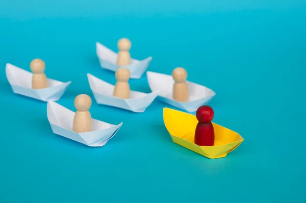 Leadership Concept - Wooden figure on yellow paper ship origami leading the rest of the figure on white paper ship. Copy space.