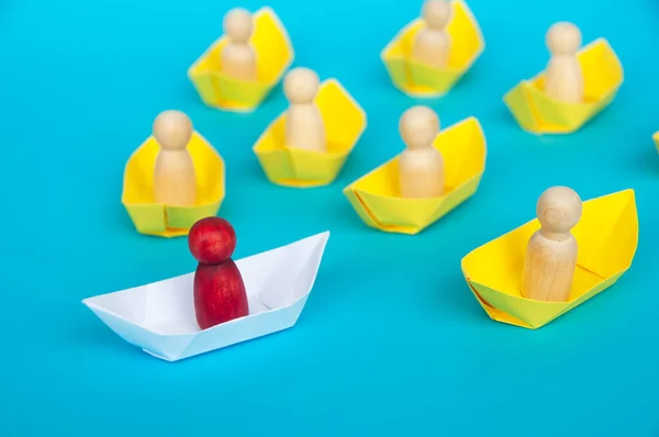 Leadership Concept - Wooden figure on white paper ship origami leading the rest of the figure on yellow paper ship. Copy space.