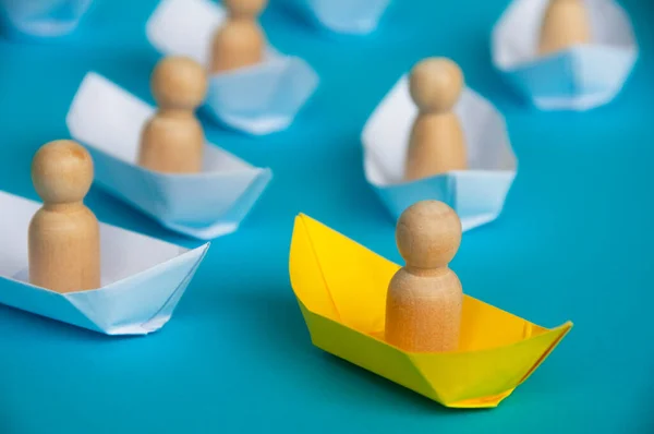 Leadership Concept - Wooden figure on yellow paper ship origami leading the rest of the figure on white paper ship. Copy space.