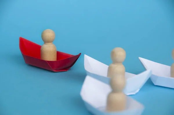 Leadership Concept - Wooden figure on red paper ship origami leading the rest of the figure on white paper ship. Copy space.