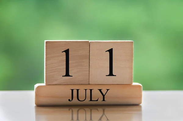 July 11 calendar date text on wooden blocks with blurred background park. Copy space and calendar concept