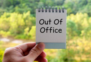 Out of office text on calendar desk with blurred nature background. Out of office concept