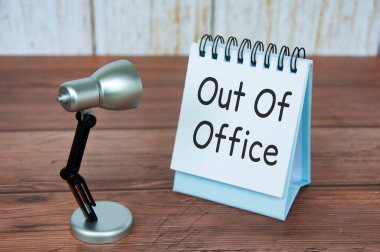 Out of office text on calendar desk with table lamb on wooden background. Out of office concept