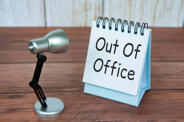 Out of office text on calendar desk with table lamb on wooden background. Out of office concept