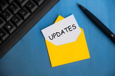 Updates text on a piece of paper in an envelope. With keyboard and pen on blue background.Business updates concept