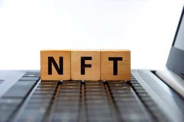 NFT represent Non-Fungible token text on wooden blocks on top of laptop. Cryptocurrency concept.