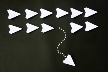 White paper plane origami leaving other white planes on dark background. Leadership skills concept.
