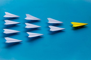 Yellow paper plane origami leading white planes on blue background. Leadership skills concept.