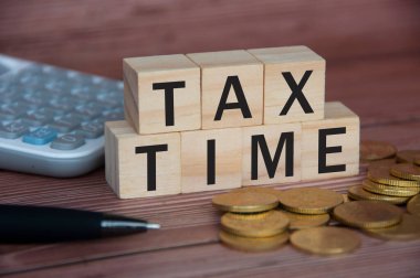 Tax time text on wooden blocks with gold coins, pen and calculator. Tax concept.