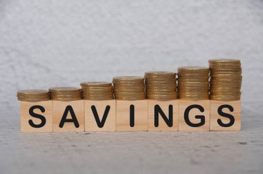 Savings text on wooden blocks with gold coins on top. Save money concept.