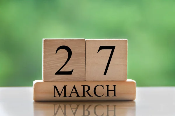 March 27 calendar date text on wooden blocks with blurred park background. Copy space and calendar concept.