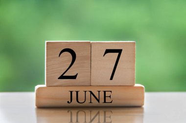 June 27 calendar date text on wooden blocks with blurred nature background. Copy space and calendar concept.