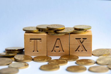 Tax word engraved on wooden block surrounded with gold coins. Taxation concept.