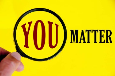 Hand holding magnifying glass with text You matter on yellow cover background. Motivational concept.